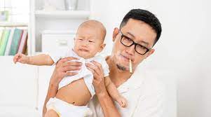 Father smoking with the crying baby in his arms.